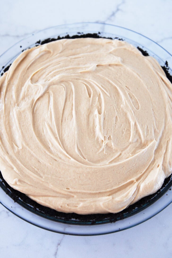Top down view of a creamy peanut butter pie over an Oreo crust in a glass pie pan.