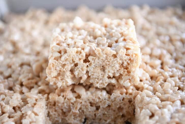 A pan of rice krispies with one treat stacked on top of the pan of treats.