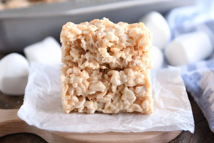 Two rice krispie treats stacked on top of each other on a piece of parchment. The top one has some bites taken out.