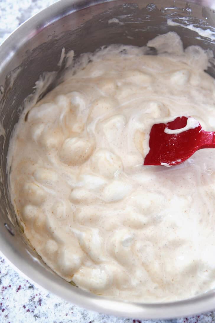 Top down view of a metal pan with melted marshmallows and butter being stirred with a red spatula.