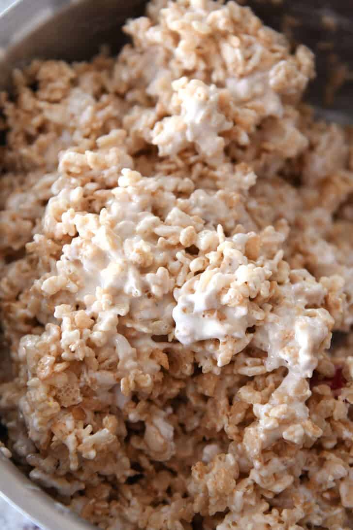 Rice krispie treat mix being stirred together in a metal pot.