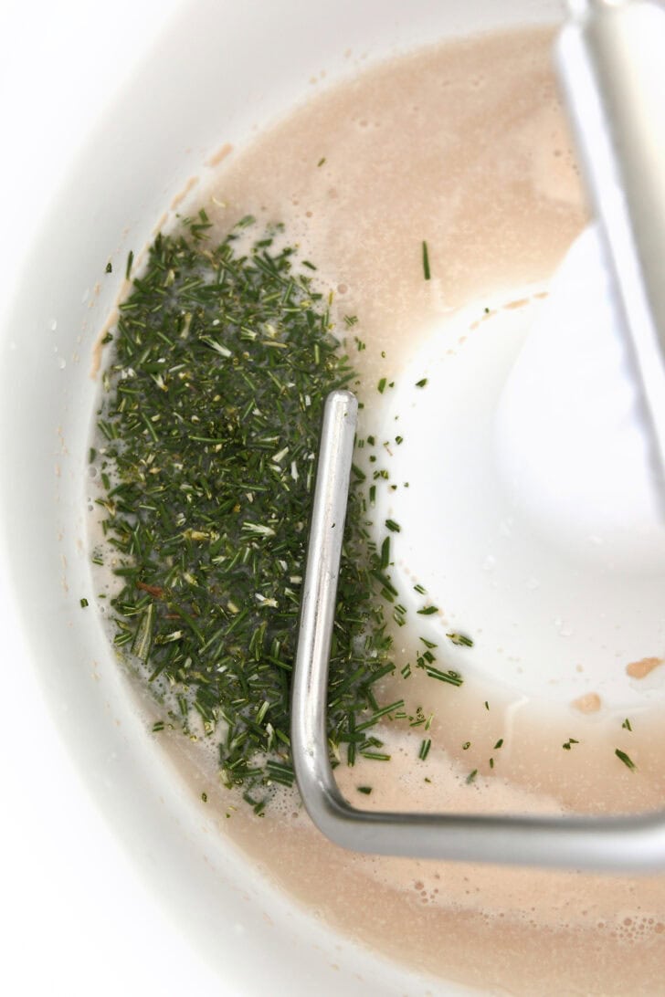 Top down view of a mixing bowl with a yeast and chopped rosemary mixture.