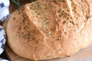 Top down view of a golden brown loaf of rosemary bread on a cutting board.
