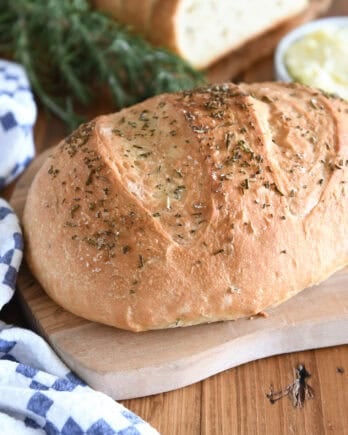 Top down view of a golden brown loaf of rosemary bread on a cutting board.