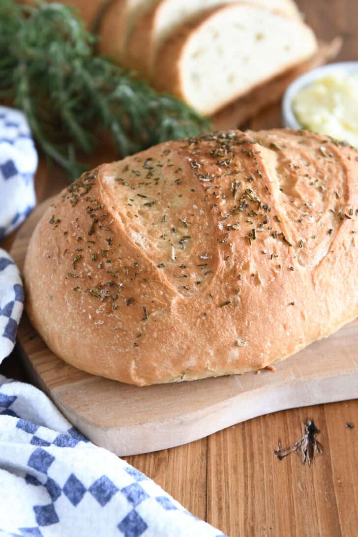 Top down view of a golden brown loaf of rosemary bread on a cutting board.