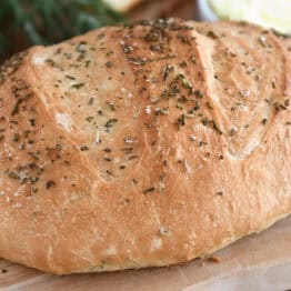 A golden brown loaf of rosemary bread on a cutting board.