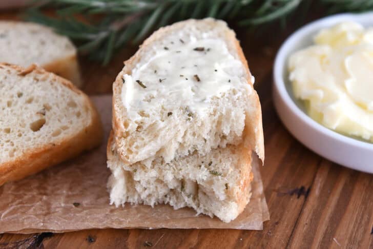 A thick slice of rosemary bread slathered with butter stacked on another half piece of bread.