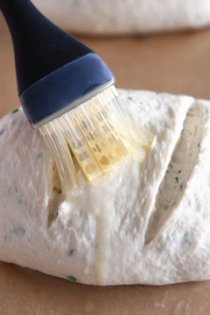 An uncooked loaf of bread dough getting melted butter brushed on top.