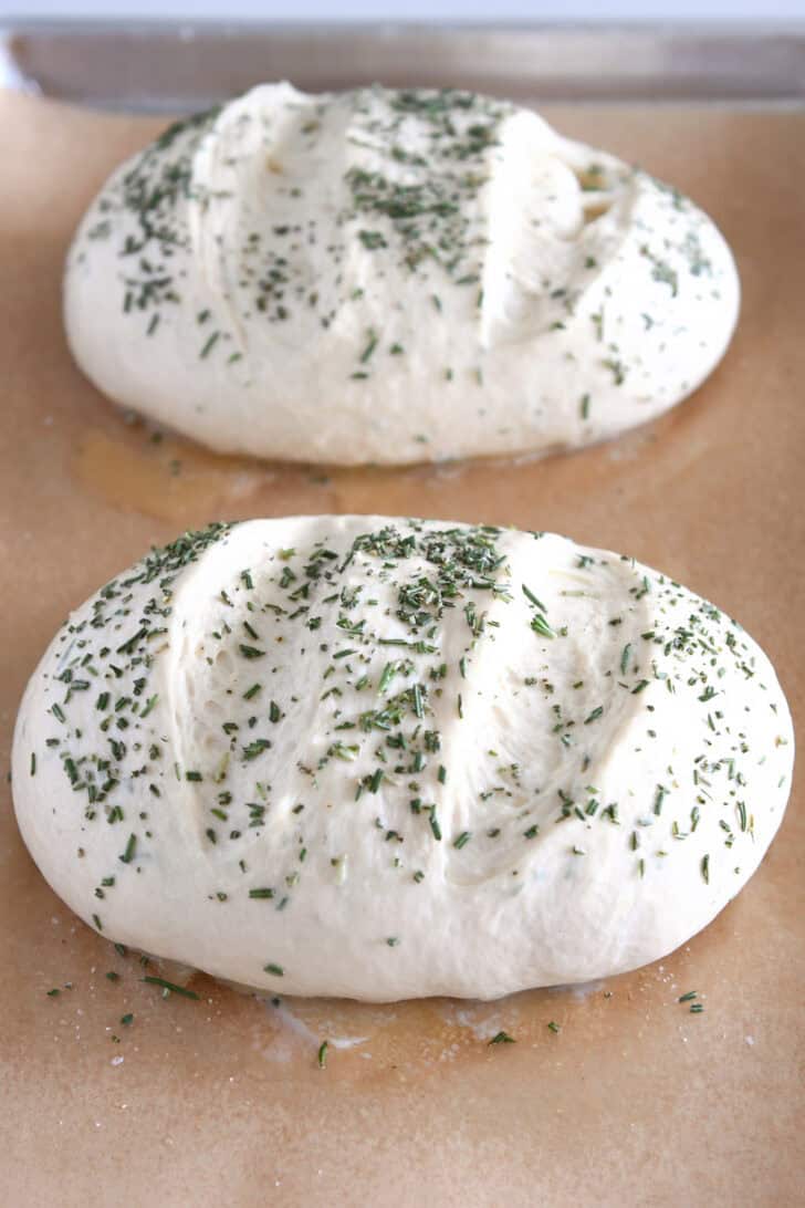Loaves of uncooked bread dough with sprinkled rosemary on them.