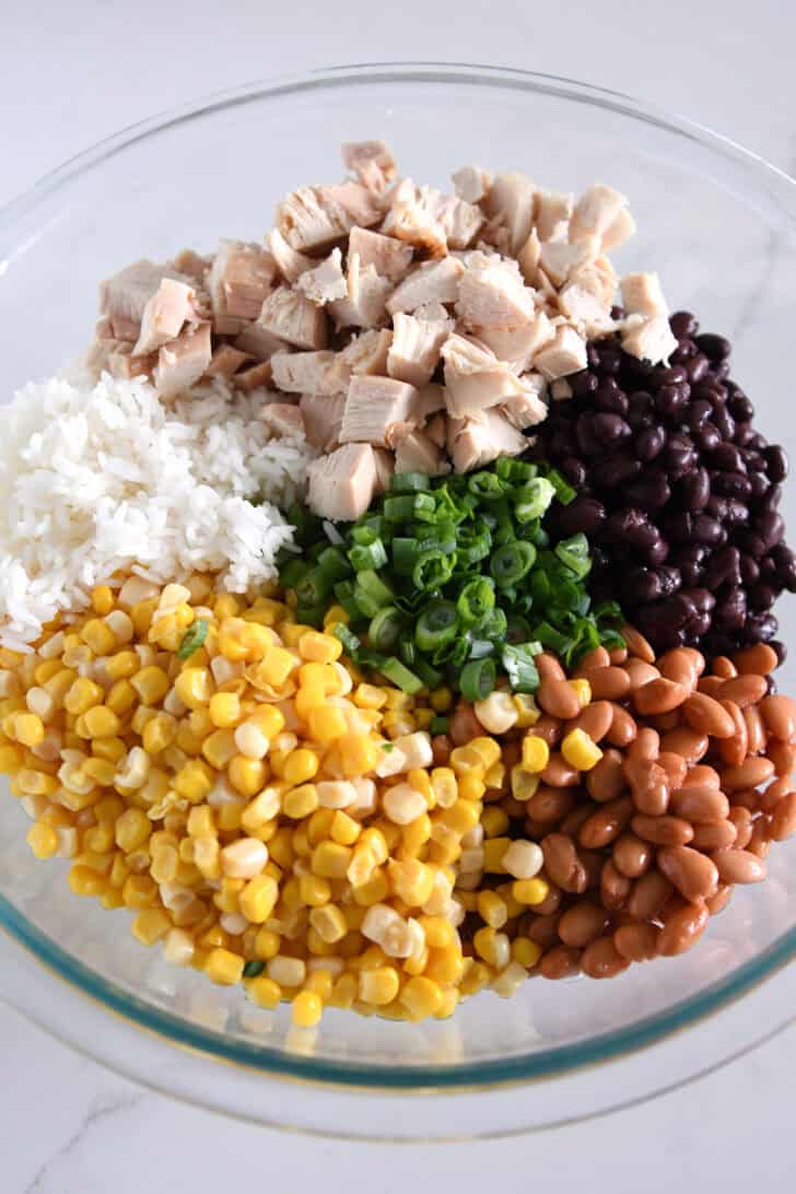 Top down view of a glass bowl with rice, chicken beans, corn and green onions.