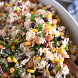 Top down view of a white dish with a rice, bean, and chicken salad topped with chopped cilantro.