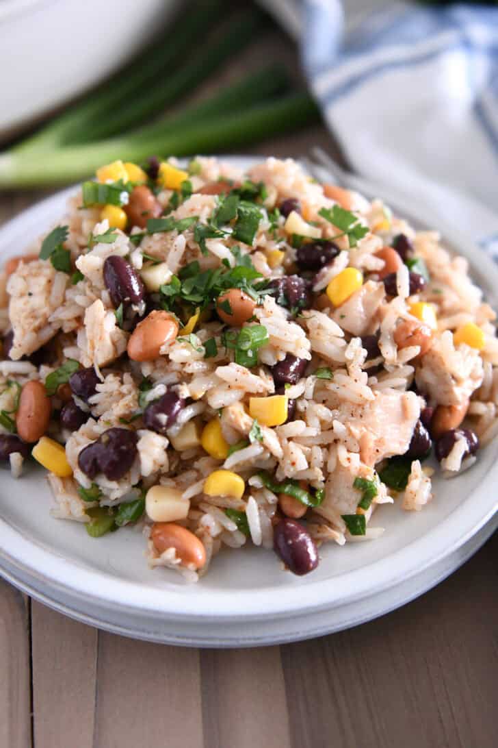 A white plate with a rice, bean, and chicken salad topped with chopped cilantro.