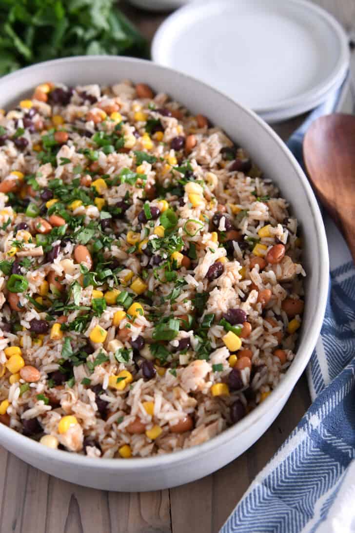 Top down view of a white oval dish with a rice, bean, and chicken salad topped with chopped cilantro.