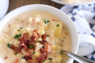 White bowl with spoon scooping up chowder with fresh corn, bacon, potatoes and carrots.