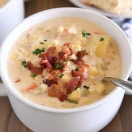 White bowl with spoon scooping up chowder with fresh corn, bacon, potatoes and carrots.