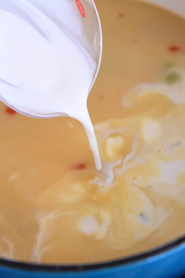 Pouring half and half into pot with chicken broth and vegetables.
