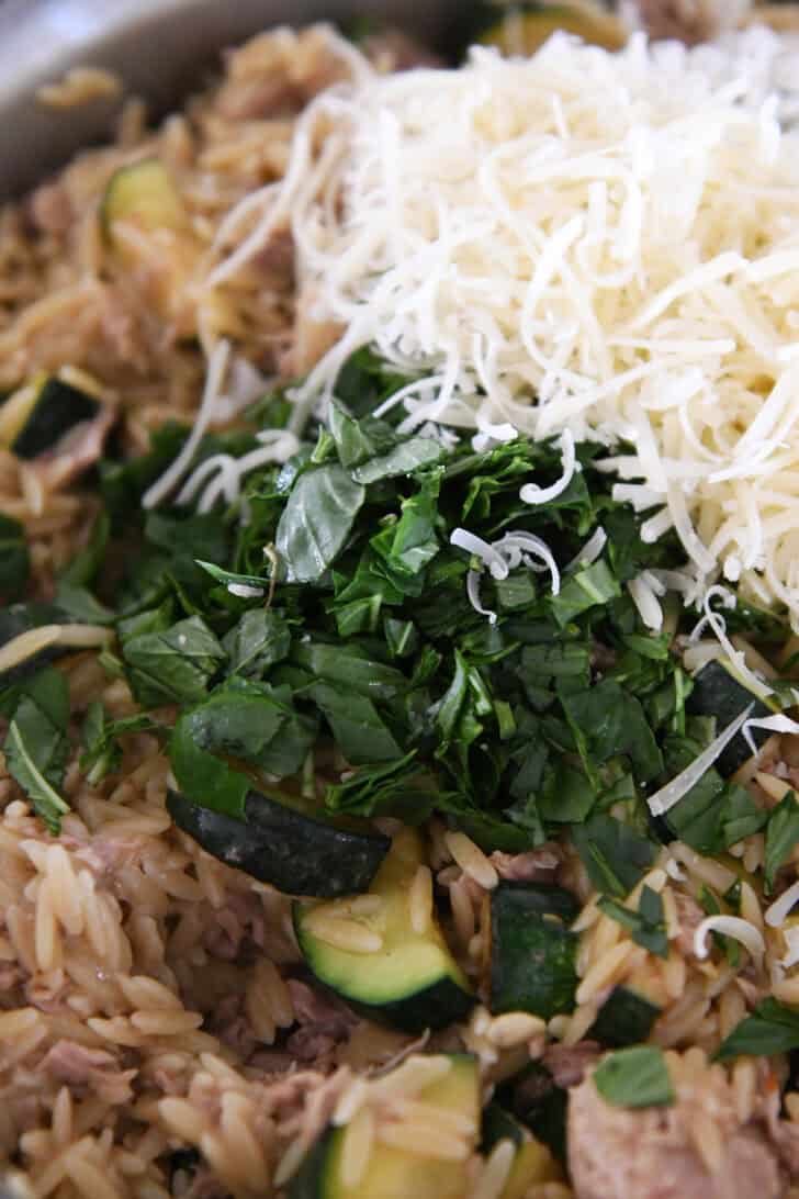 Fresh basil and Parmesan cheese on top of tuna, zucchini and orzo in stainless skillet.