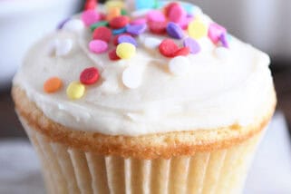 A white cupcake with white frosting and colored sprinkles.