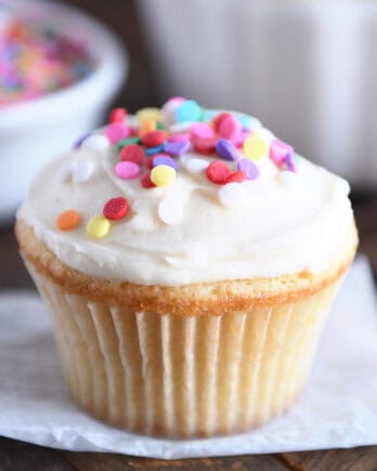 A white cupcake with white frosting and colored sprinkles.