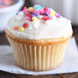 A white cupcake with white frosting and colored sprinkles.