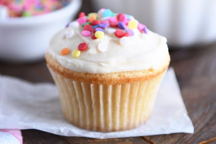 A white cupcake with white frosting and colored sprinkles.