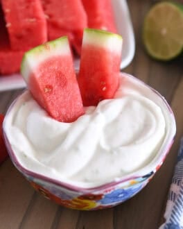 Two watermelon sticks dipped in Greek yogurt creamy watermelon dip.