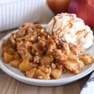 Serving of caramel apple crisp on gray plate with ice cream also drizzled with caramel.
