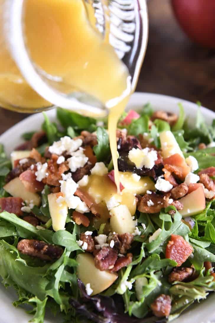 Pouring Apple Ciders Vinaigette over the green salad with chopped apples, feta cheese, pecans and bacon.