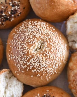 Top down view of sesame seed topped bagel with several other baked bagels.