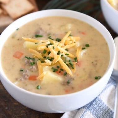 White bowl with creamy cheesy soup with cooked potatoes, carrots and ground beef topped with shredded cheddar cheese and chopped chives.