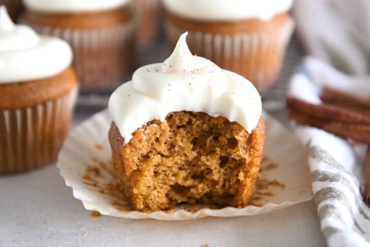 Pumpkin Cupcake topped with Whed Cream Charse Cheese Frosting with a bite cut out of a Cupcake Liner.