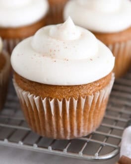 Several pumpkin cupcakes topped with whipped cream cheese frosting on wire cooling rack.