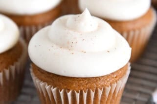 Several pumpkin cupcakes topped with whipped cream cheese frosting on wire cooling rack.