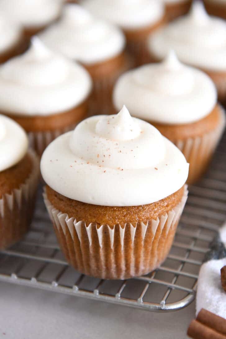 Many Pumpkin Cupcakes are arranged with Whed Cream Cheese Frosting on a Wire Cooling Rack.