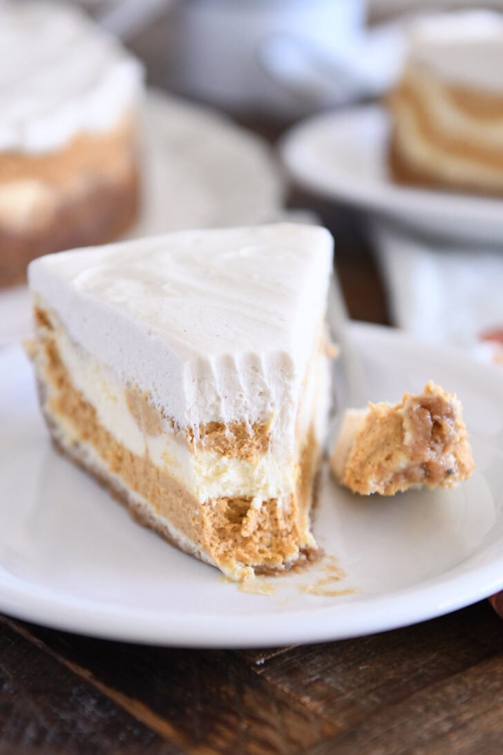 Slice of pumpkin swirl cheesecake with bite removed on white plate.