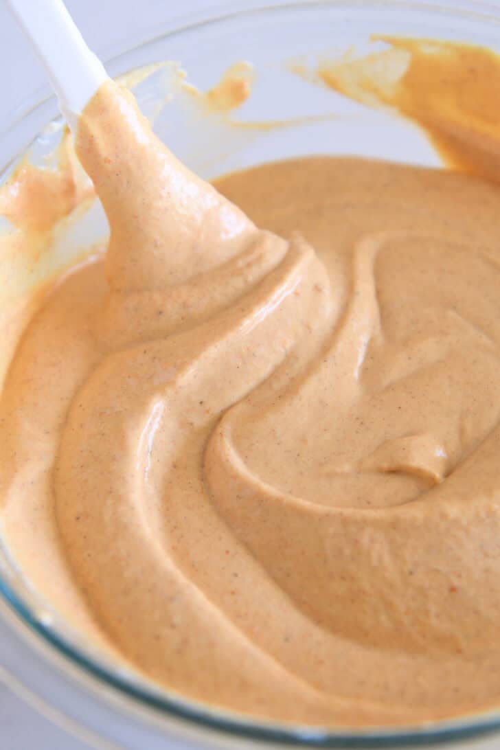 Pumpkin cheesecake batter in glass bowl with white spatula.