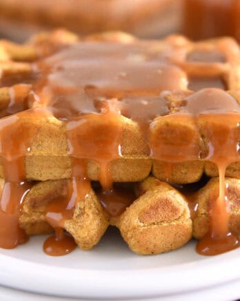 Two squares of pumpkin waffles on white plate smothered in buttermilk caramel syrup.