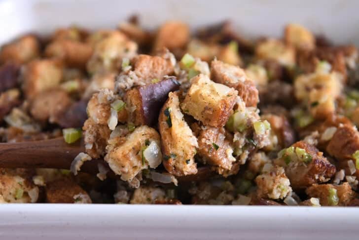 Spoon scooping serving of baked sausage and herb stuffing.