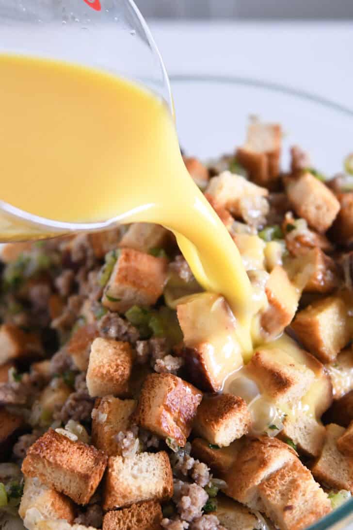 Pouring blended eggs and broth into dried bread cubes, sausage and herbs.
