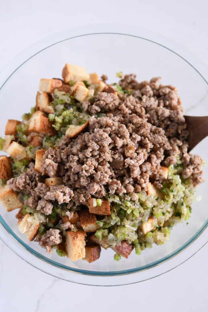 Glass bowl with toasted bread cubes, cooked vegetables and cooked sausage.