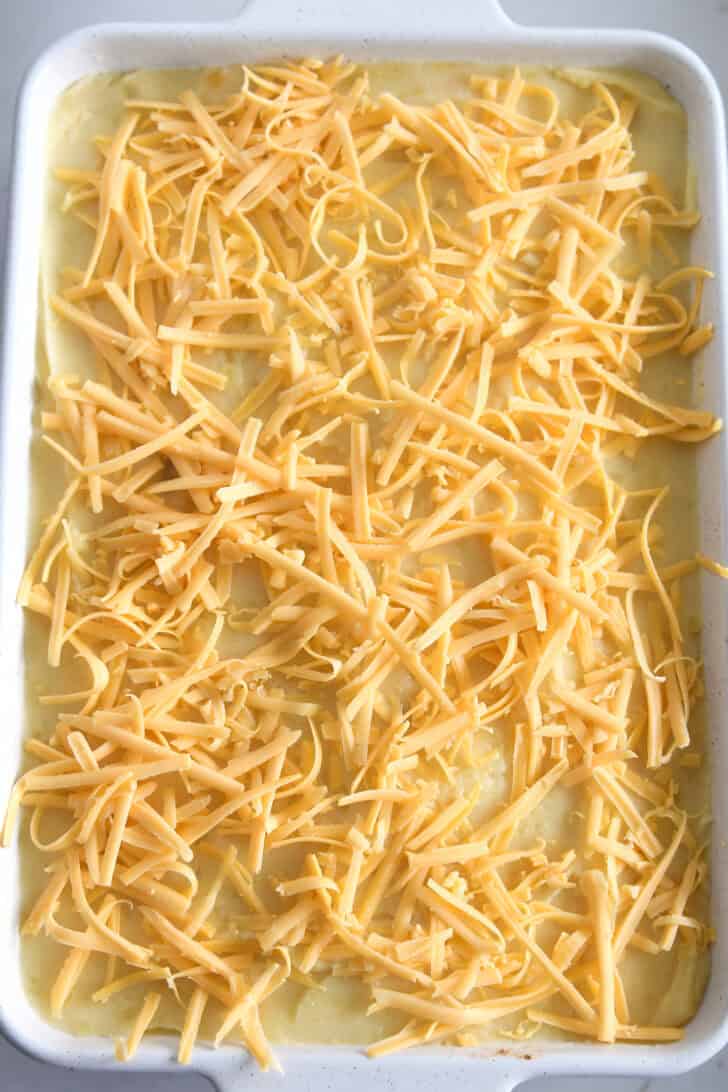 Top down view of a white casserole dish with mashed potatoes and shredded cheese on top.