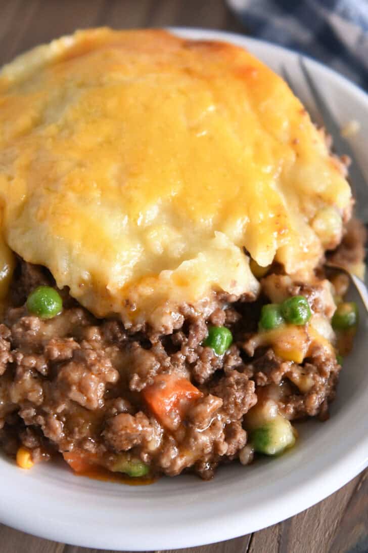 A beef and vegetable mixture topped with cheesy potatoes in a white bowl.