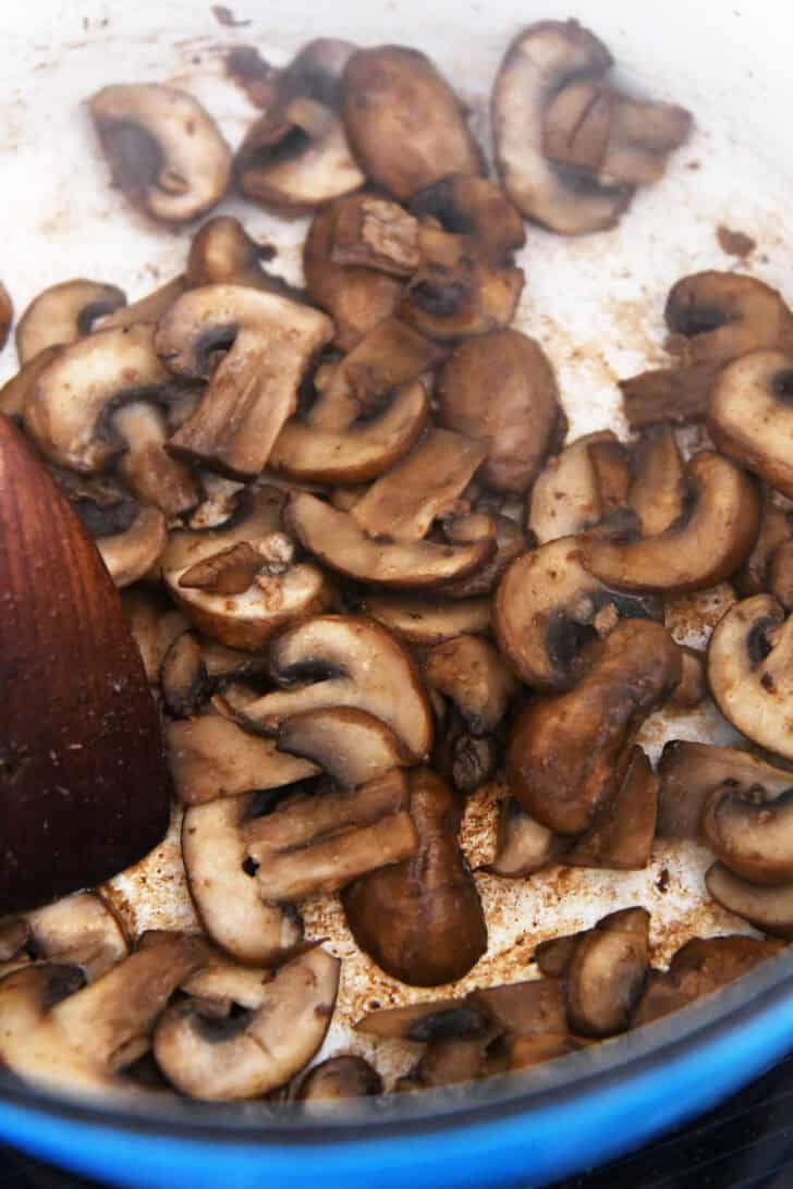 Top down view of a pot of sliced mushrooms being sautéed.