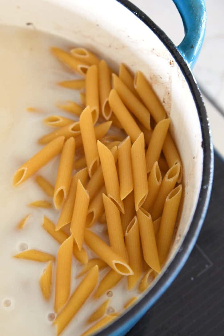 Top down view of a pot with uncooked penne pasta in a white sauce.