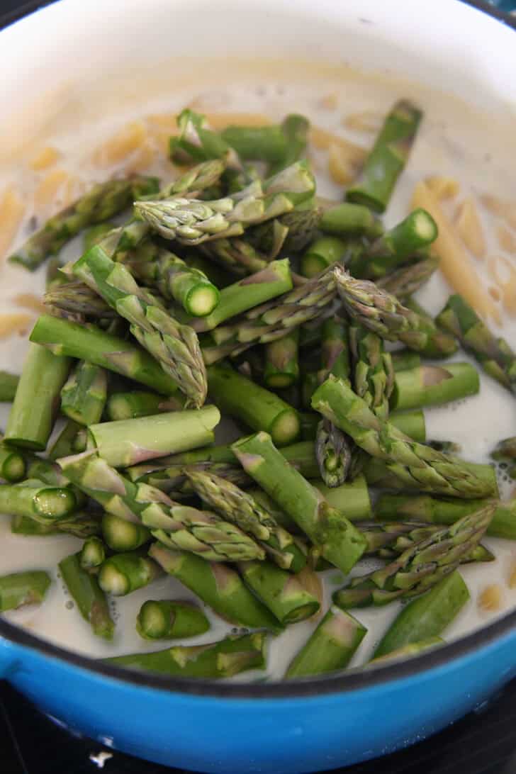 Top down view of a pot with penne pasta in a white sauce all topped with chopped asparagus.