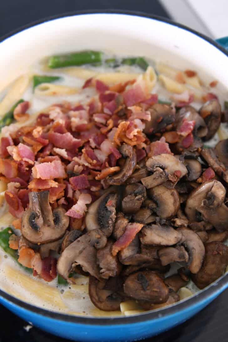 Top down view of a pot with a creamy pasta sauce topped with crumbled bacon and sliced mushrooms.