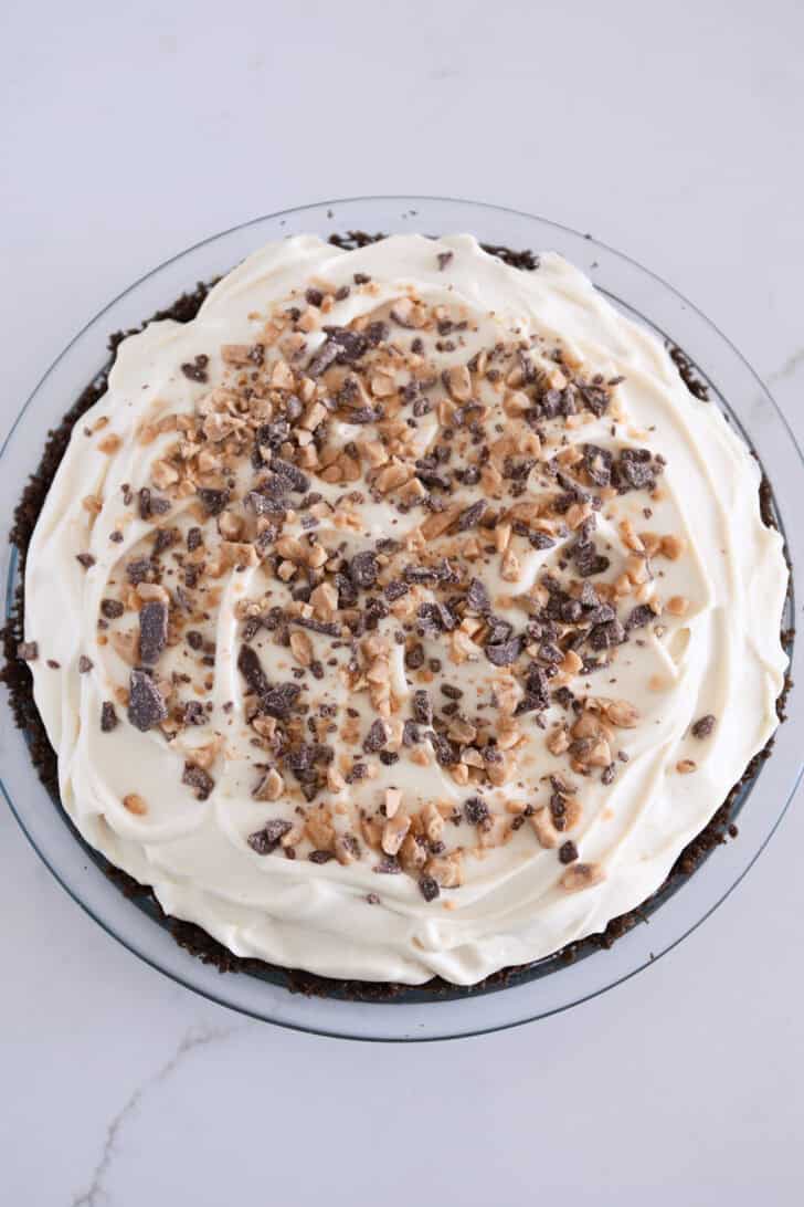 Chocolate covered toffee bits sprinkled across the top of whipped cream covered pie.