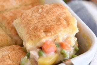 Spoon lifting out scoop of chicken pot pie filing for white 9X13-inch pan with baked biscuit on top.