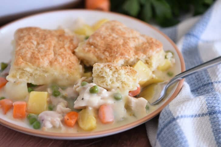 Fork scooping bite of chicken pot pie with small piece of baked biscuit.