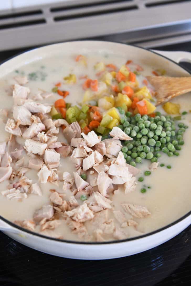 Cast iron pan filled with white sauce, cooked chicken, peas, potatoes, carrots and celery.